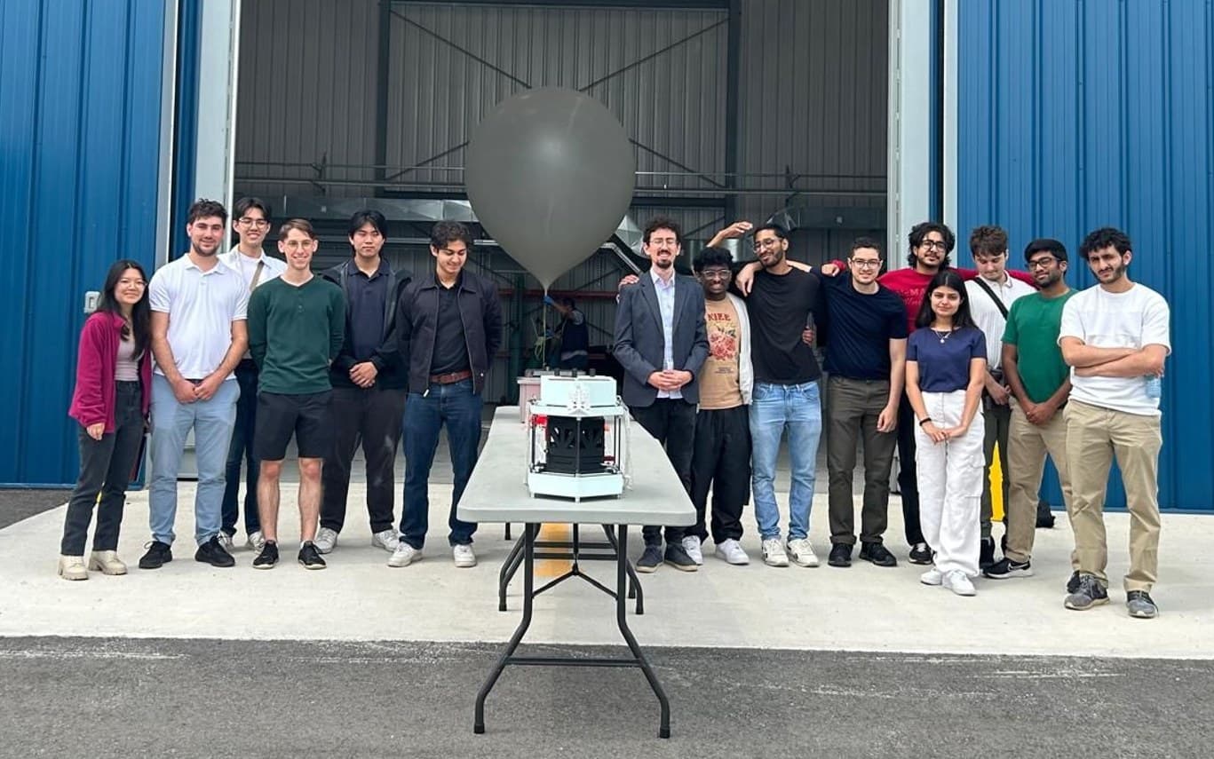 The CAN-SBX 2024 team standing behind a table with their payload, a weather balloon behind them